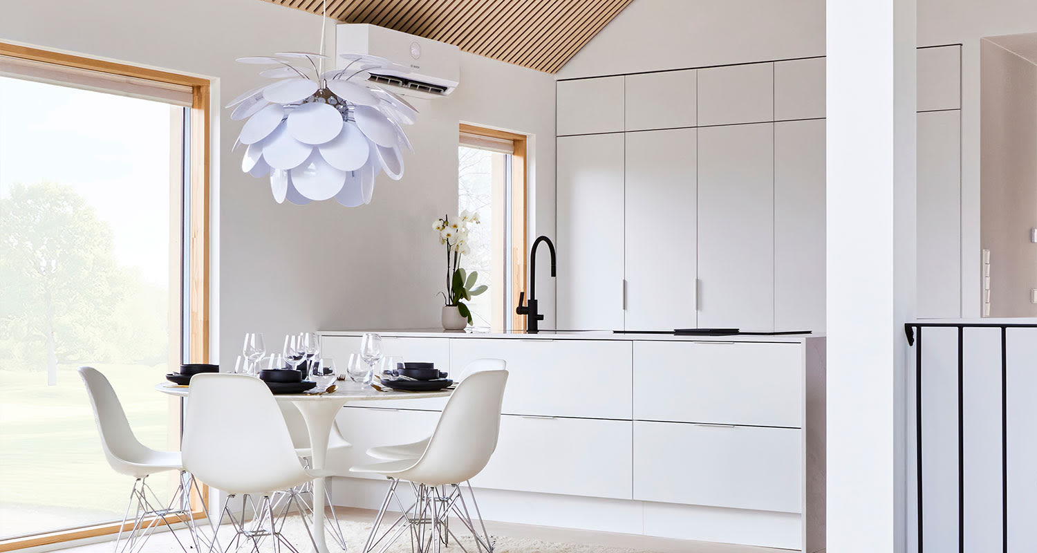 Valoisa valkoinen keittiö-ruokailutila ikkunalla, pyöreä pöytä, valkoiset tuolit, mustat astiat