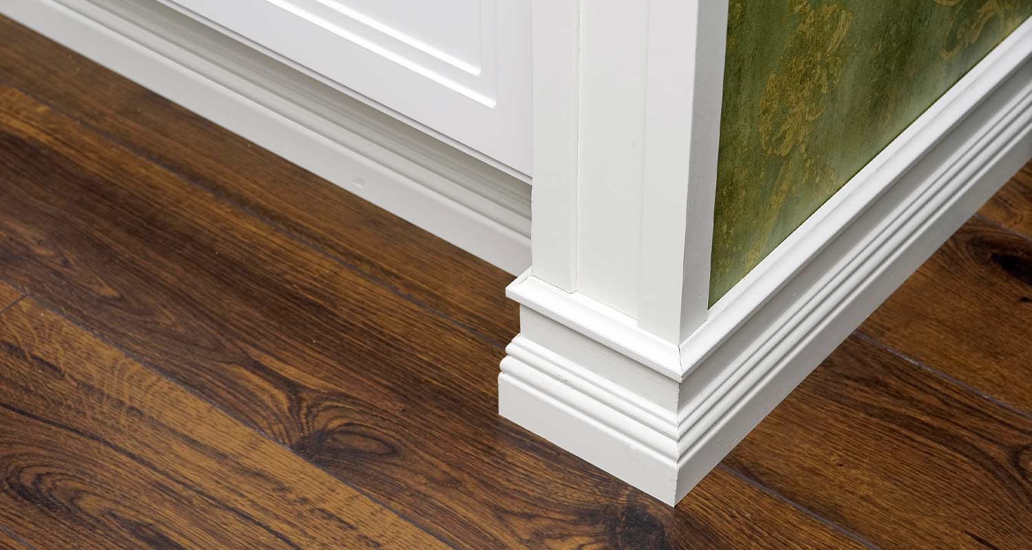 Valkoinen listoitus ja pilasteri tumman ruskean parketin ja vihreän tapetin vieressä