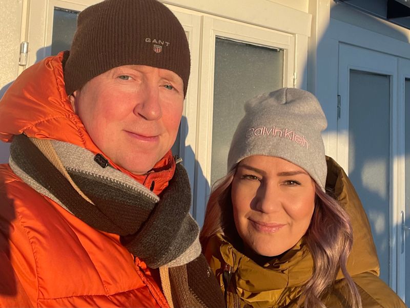 Oranssi- ja oliivinvihreät toppatakit ja pipot valkoista ovea vasten talvisessa auringossa.