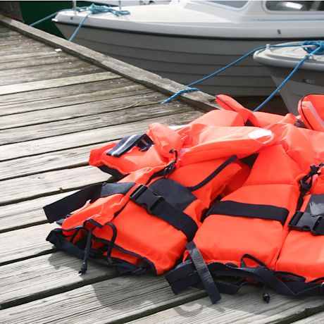 Kirkkaan oransseja pelastusliivejä puisella laiturilla sidottujen veneiden vieressä