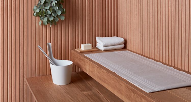 Saunan vaalea puupaneeli, penkillä valkoinen löylykauha ämpärissä, pyyhkeet ja saippua.