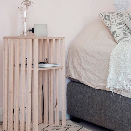 Vaalea puupöytä kuivikukkamaljakolla, beige peitto ja harmaa sängynrunko