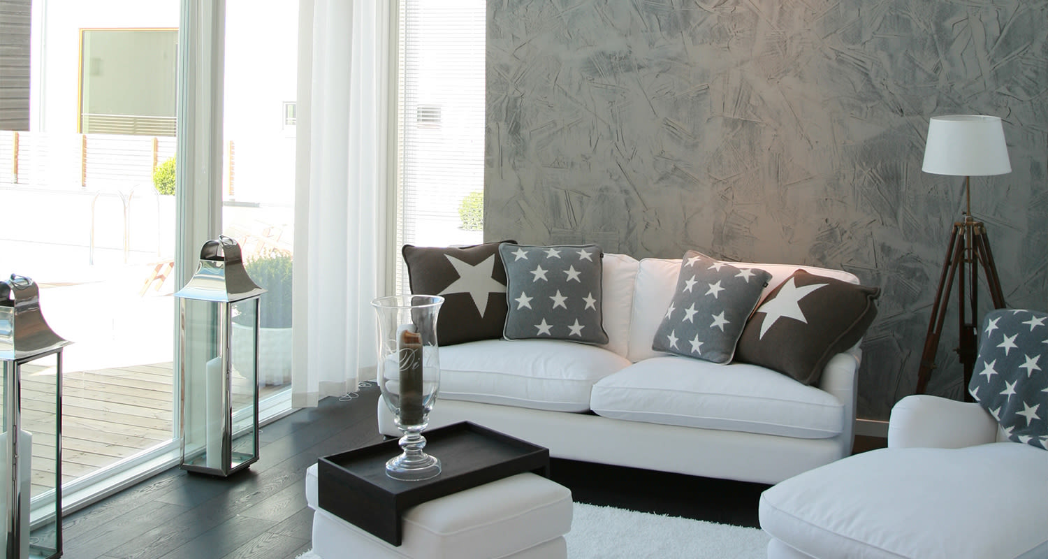 Moderni olohuone, valkoinen kulmasohva harmailla tähtityynyillä, tumma puulattia, betoniseinä