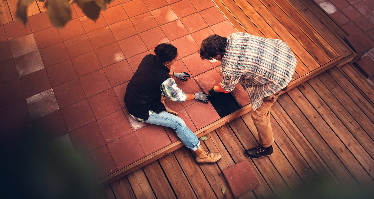 Nainen ja mies rakentamassa terassia, jossa punertavaa ulkolaattaa ja terassipuuta