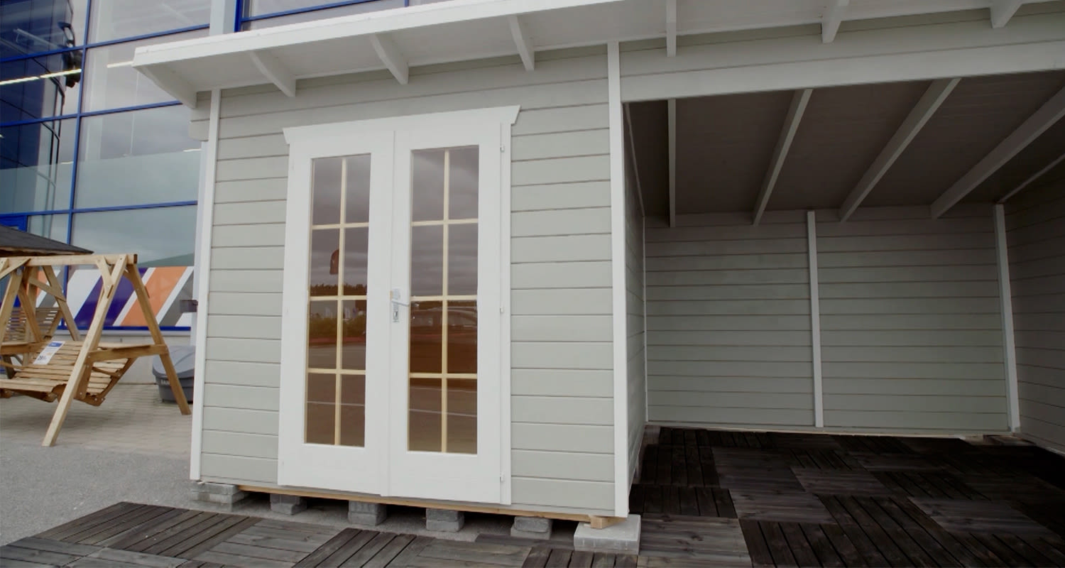 Vaaleanharmaa pihavarasto valkoisilla lasiovilla, tumma puulattia kaupan edustalla