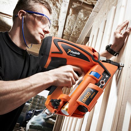 Rakennustyömies kiinnittää puupaneelia oranssilla Paslode-naulakoneella