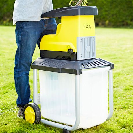 Ihminen työntää oksia keltamustaan puutarhakutteriin nurmikolla.