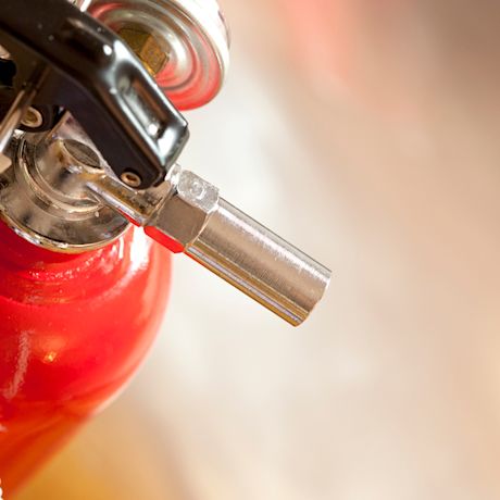 Punaisen palosammuttimen metallinen suutin ja musta kahva lähikuvassa.