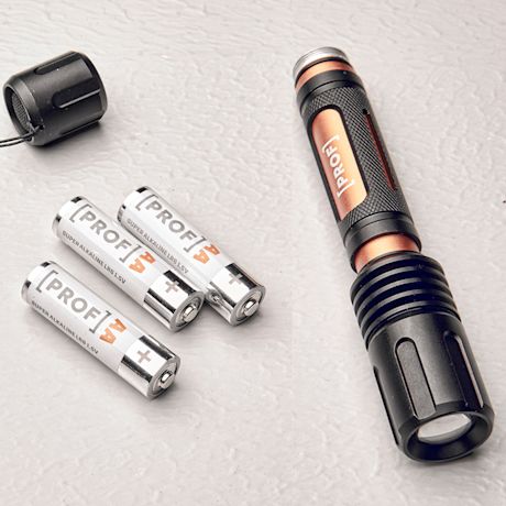 Musta-oranssi metallinen taskulamppu ja kolme valkoista PROF AA-paristoa vaalealla pinnalla