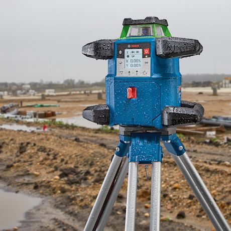 Sininen ja vihreä Bosch-laser jalustalla märällä rakennustyömaalla.