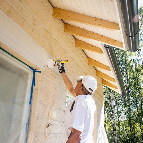 Mies maalaa omakotitalon puuseinää valkoiseksi
