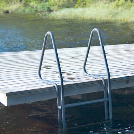 Vaalea puulaituri ja harmaat tikkaat tummassa järvivedessä taustalla vihreää kasvillisuutta