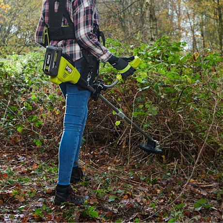 Ruudullispaitainen henkilö harmaavihreällä Ryobi-ruohoraivurilla raivaa syksyistä metsänpohjaa.