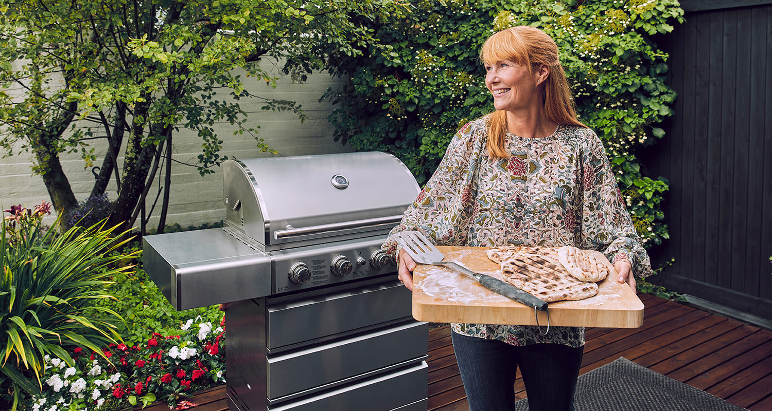 Nainen pitelee leikkuulautaa grillattujen pitaleipien ja lastan kanssa ulkogrillin edessä