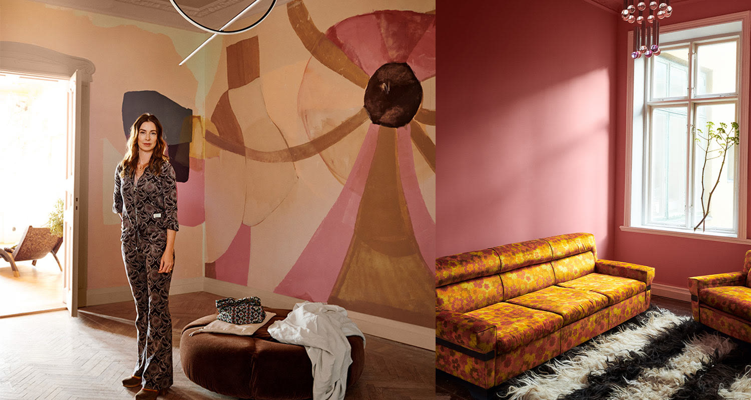 Huone jossa abstrakti vaalea seinämaalaus, kukkakuosinen keltainen sohva ja mustavalkoinen karvamatto.