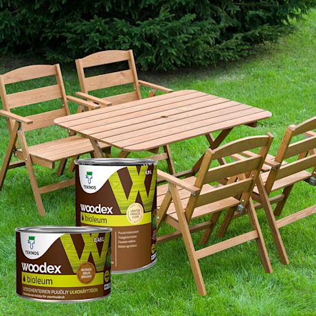 Vihreällä nurmella puinen puutarhapöytä ja tuolit, edessä kaksi ruskeaa Woodex Biooleum -öljyä.