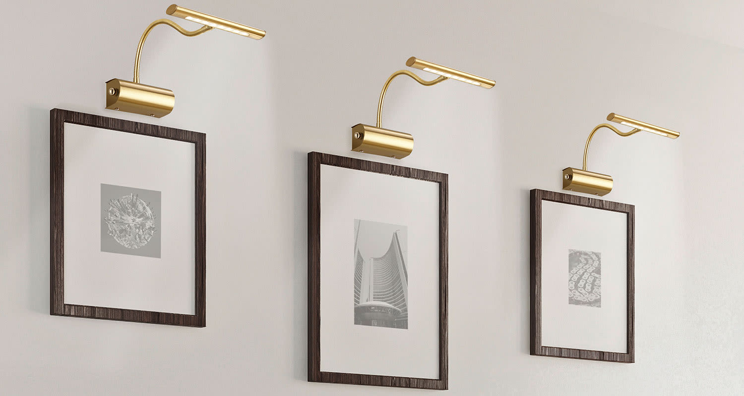 Kolme harmaasävykuvaa tummissa puukehyksissä valkoisella seinällä kultaiset lukuvalot.