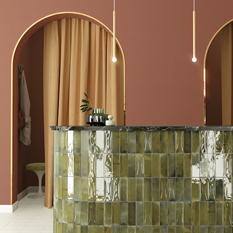 Kuvassa pyöreitä muotoja ja pehmeitä sävyjä: oliivinvihreä laatta baaritiskissä ja ruusunpunaiseen taittavaa seinää holvikaaren muotoisten oviaukkojen kera.