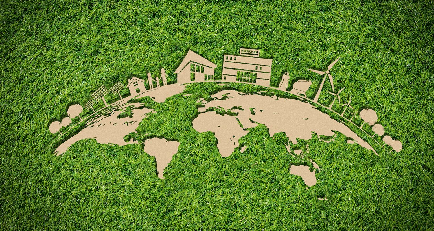 Vihreällä nurmikolla kartonkikuvioinen maailmankartta, taloja, aurinkopaneeleja ja tuulivoimaloita.