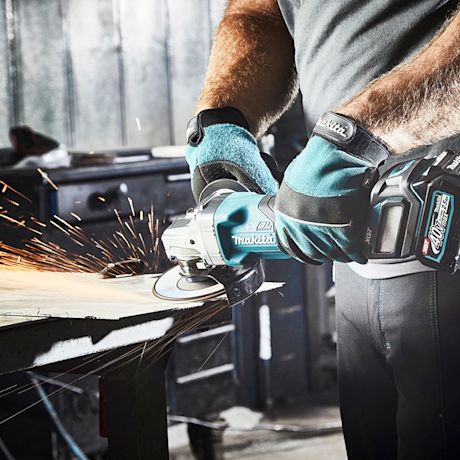 Työmies hioo metallilevyä Makita-akkuhiomakoneella, kipinöitä, turkoosit suojakäsineet