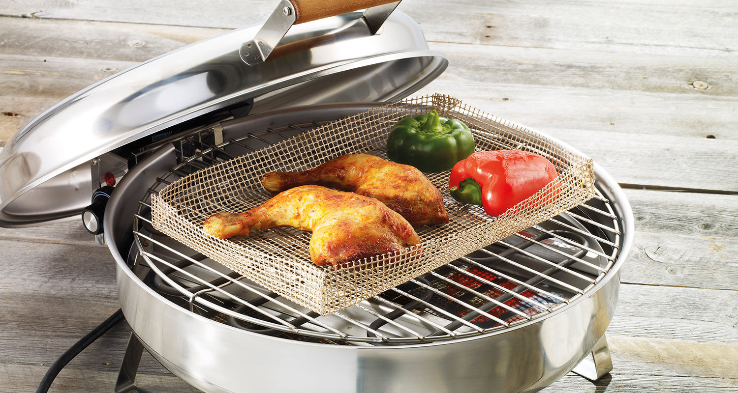 Pyöreä avoin teräsgrilli puupöydällä, verkkoräkissä kaksi paahdettua kanankoipaa, vihreä ja punainen paprika.