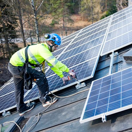 K-Aurinkovoimala ja mies asentamassa aurinkopaneeleita katolle.
