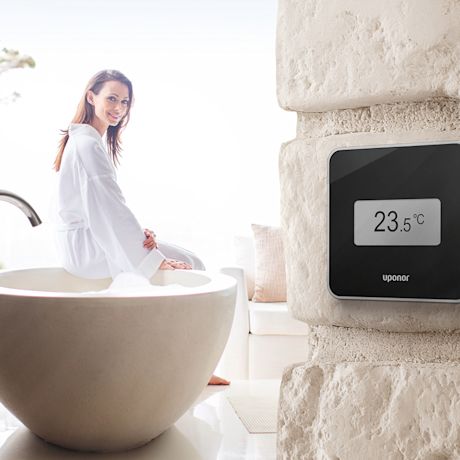 Vaalea kylpyhuone, pyöreä kiviamme, nainen kylpytakissa ja termostaatti 23,5 °C