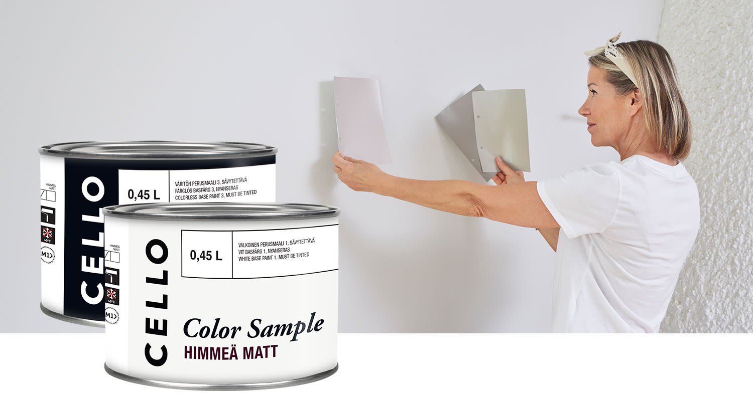 Valkopaitainen nainen asettaa seinälle harmaan ja beigen värikartan, etualalla Celo-maalinäytteet