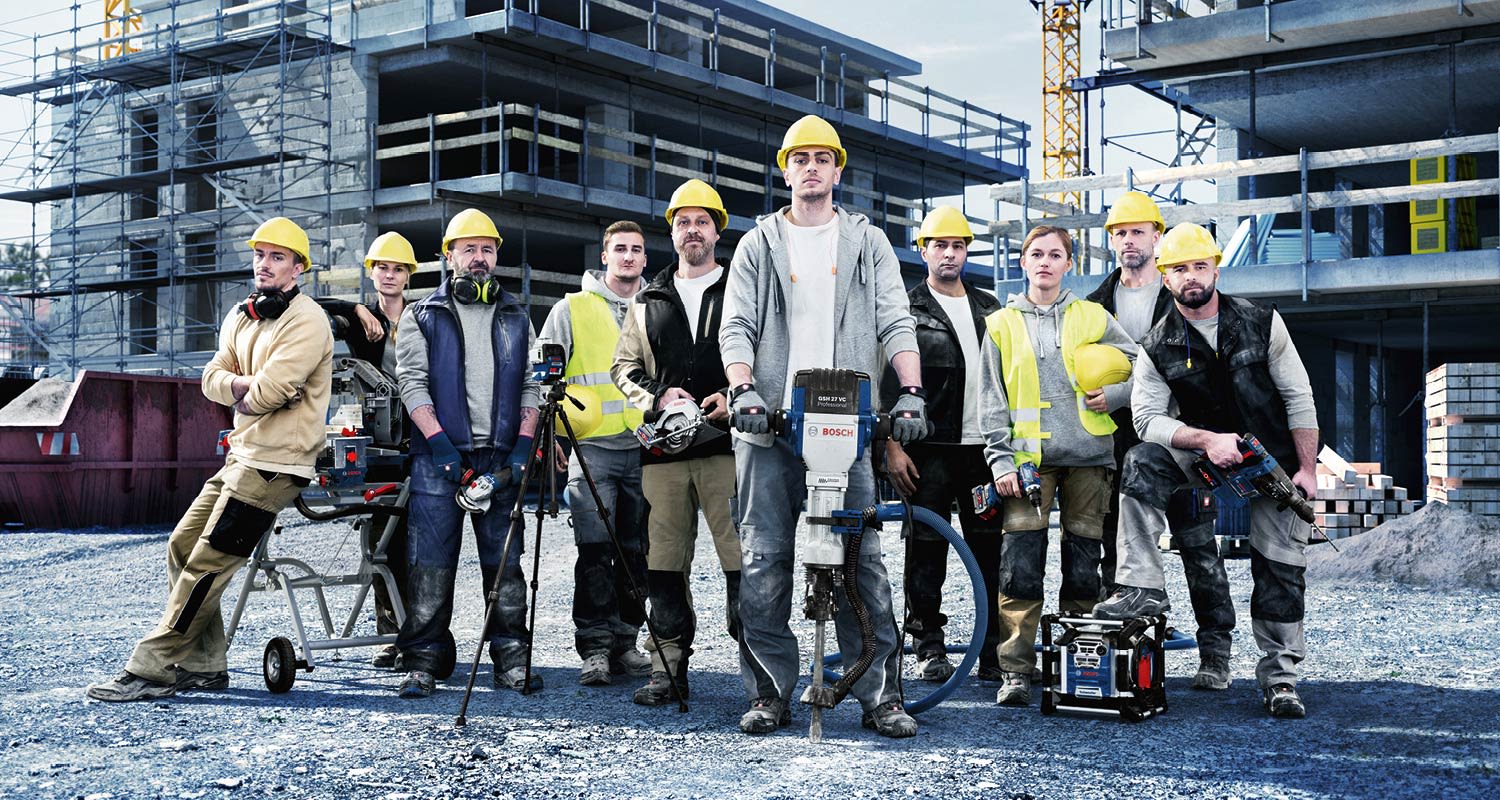 Rakennustyöläisiä keltaisissa kypärissä ja sähkötyökaluissa betonityömaalla.