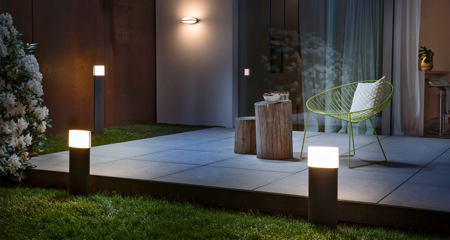 Yöterassi laattalattialla, mustat pylväsvalot, vihreä metallituoli ja puupölkyt