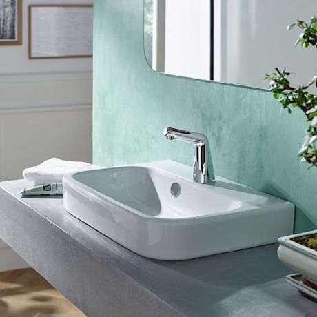 Valkoinen pesuallas harmaalla betonitasolla, kosketukseton kromihana ja peili vihreällä seinällä.