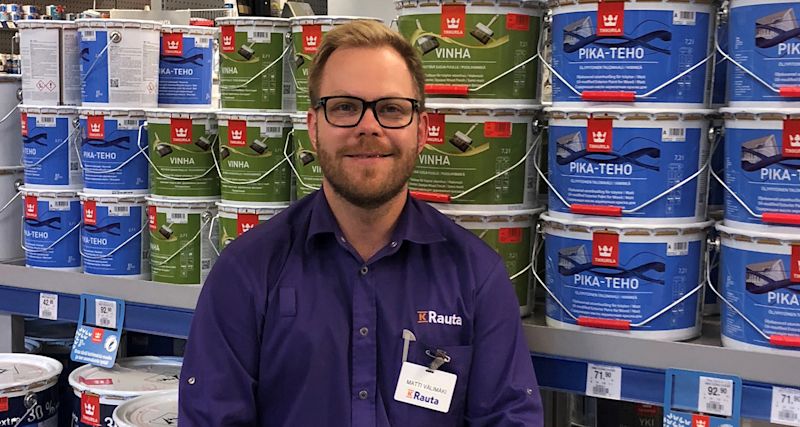 K-Raudan työntekijä sinisten ja vihreiden maalisankojen vieressä kaupan hyllyllä.