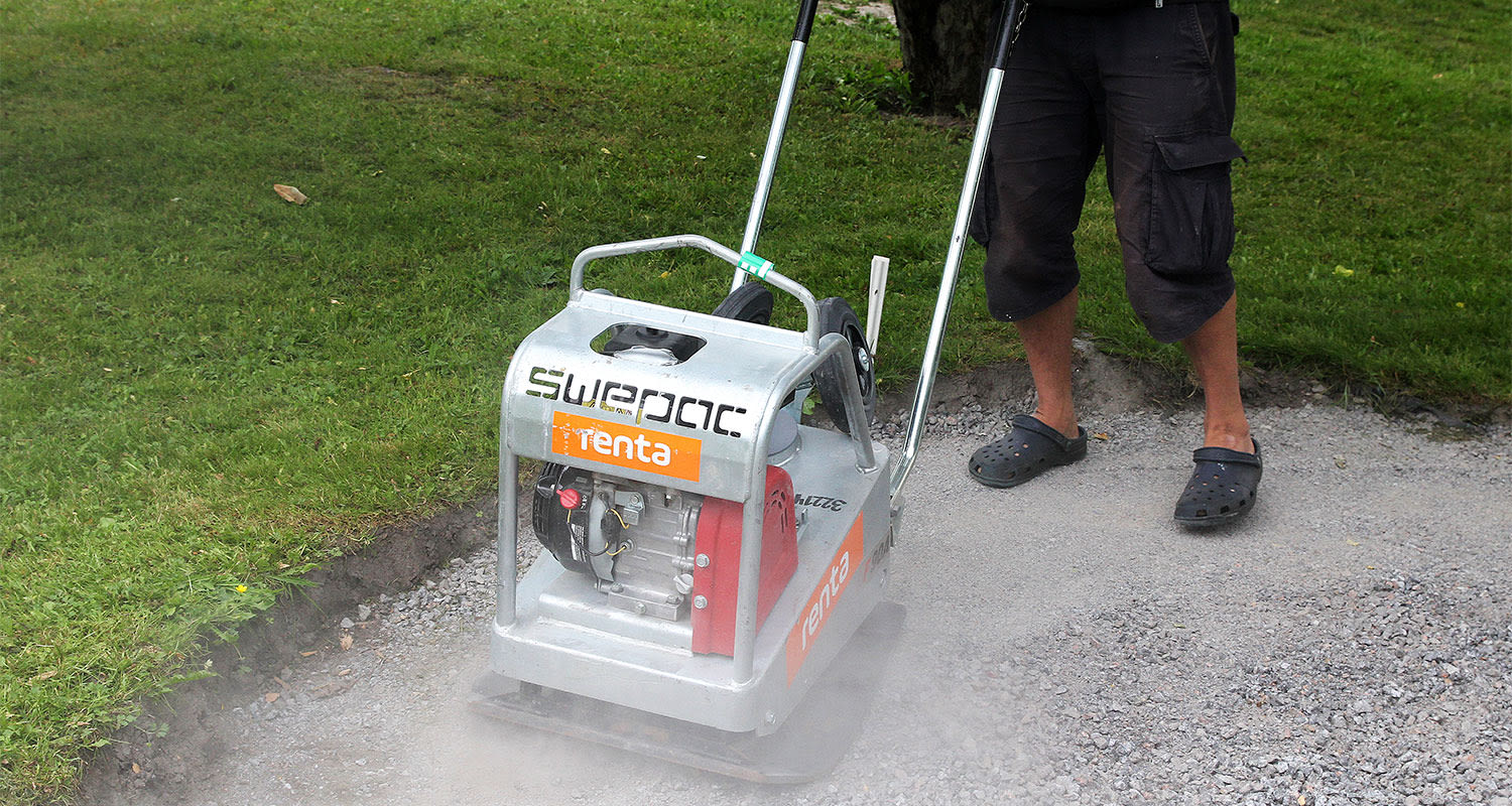 Hopeanhohtoista Renta Swapac-soratiivistäjää pölyävällä polulla, vihreä nurmi ja miehen jalat.