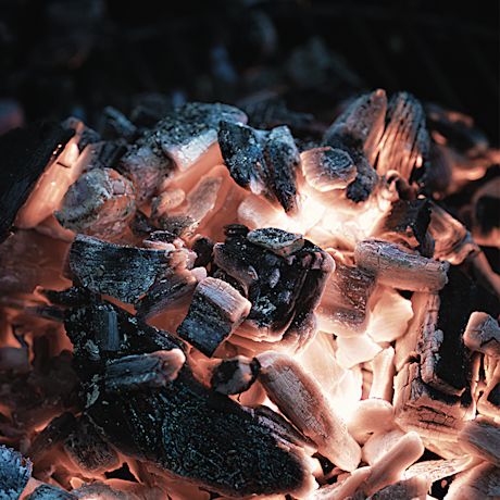 Hehkuvat oranssi-valkeat hiilet mustien tuhkaröykkiöiden keskellä.