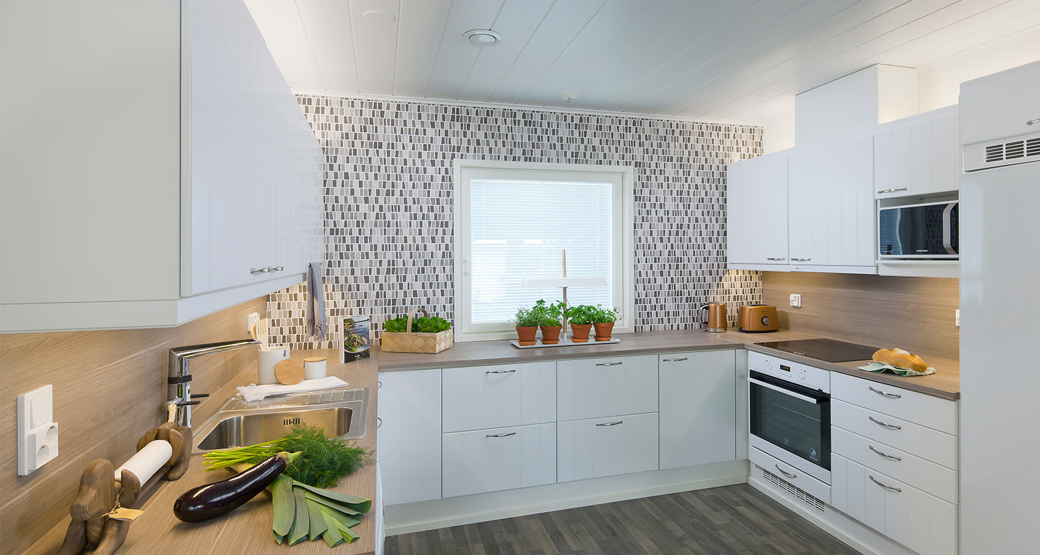 Valoisa U-muotoinen valkoinen keittiö puupinnalla, mosaiikkiseinällä ja yrttiruukuin