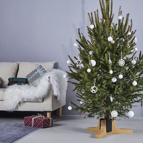 Kuvassa joulukuusi valkoisin koristein puisessa kuusenjalassa.