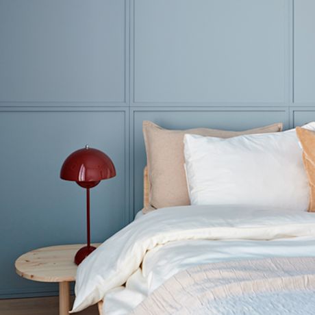Sininen paneeliseinä, puinen yöpöytä punaisella pallovalaisimella ja valkoinen sänky beigetyynyillä