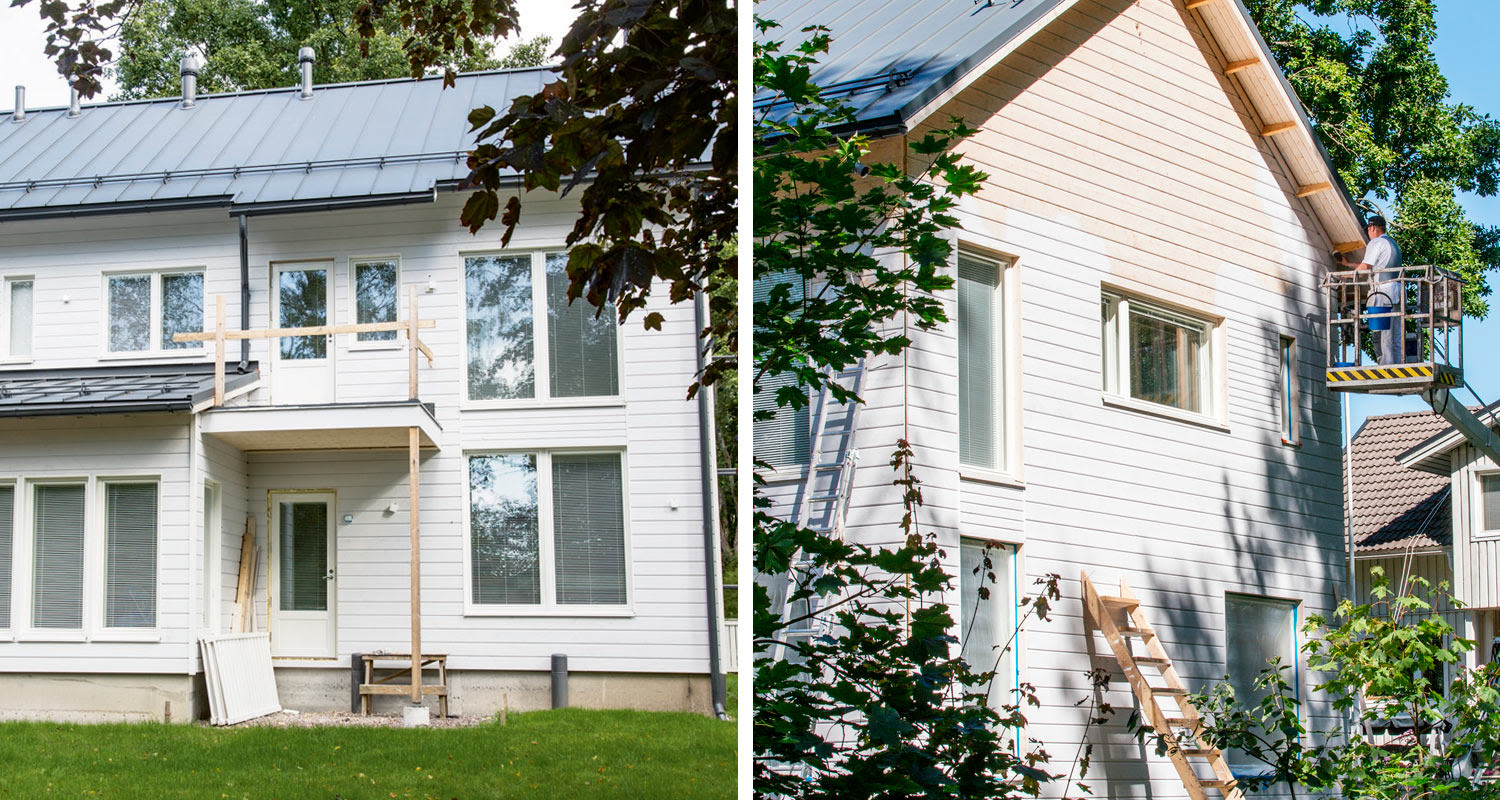 Valkoinen kaksikerroksinen puutalo maalaustöissä, työntekijä nostolavalla ja vihreitä puita edessä