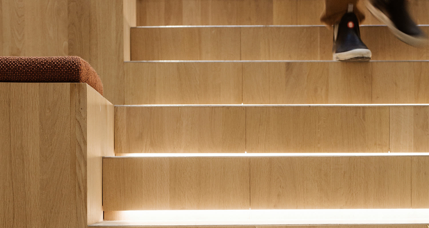 Vaaleat puuportaat integroidulla LED-valolla, punertava istuintyyny vasemmalla ja jalka yläkulmassa.