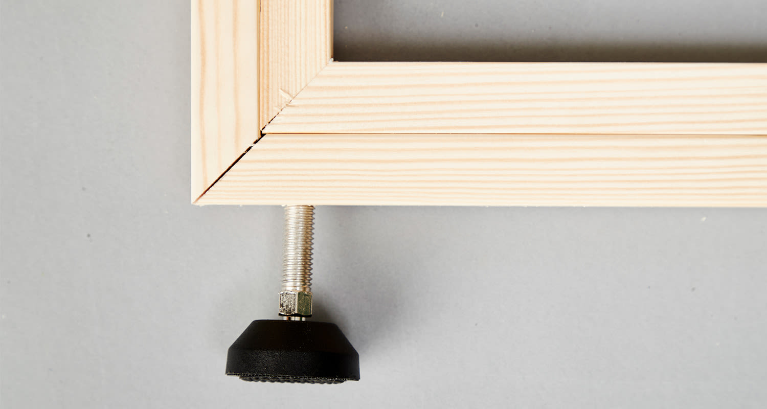 Vaalea puukehyksen kulma ja säädettävä metallijalka mustalla kumipäällä harmaalla taustalla