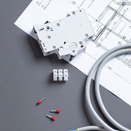 Valkoinen sähkökatkaisija piirustuspaperin päällä, harmaa kaapeli ja punaiset johdinholkit