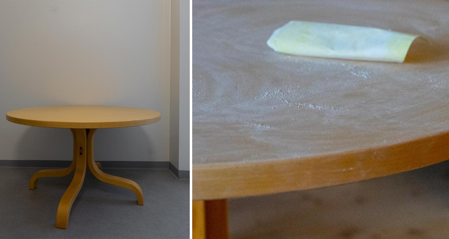 Vaalea pyöreä puupöytä nurkassa, lähikuva pinnasta ja vaalea vihreä paperinpalanen.