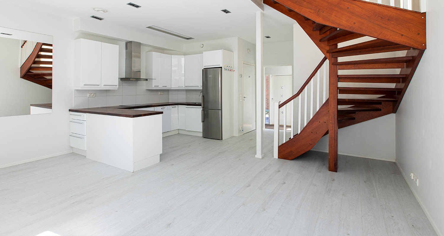 Valkoinen avokeittiö rst-jääkaapilla, tumma puuporras ja vaalea lattia