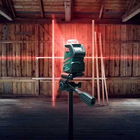 Bosch-lasertasoittimen jalustalla hehkuvat punaiset ristiinlaserlinjat puuhirsiseinässä
