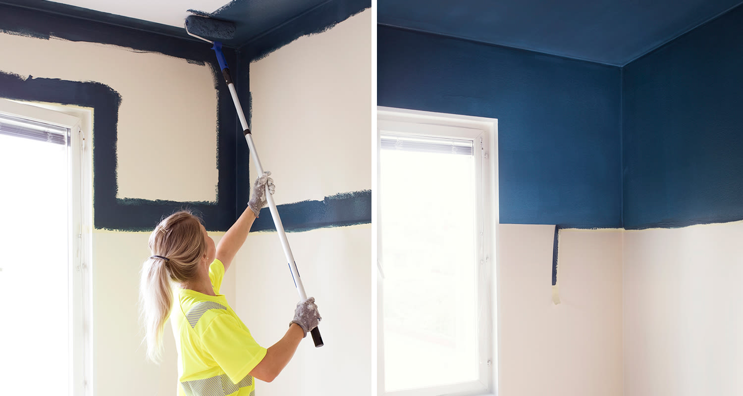 Nainen maalaa seinän yläosan tummansinistä rullalla, alapuoli valkoinen, ikkunasta valo.