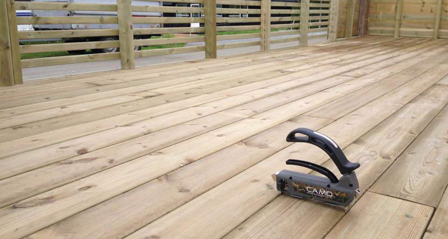 Vaaleasta puusta tehty terassilattia ja mustaharmaa CAMO-kiinnitystyökalu laudoilla.