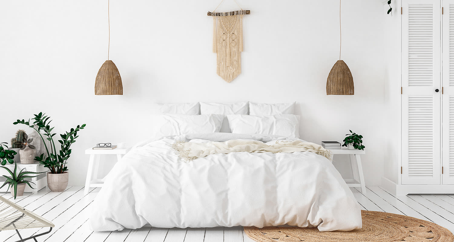 Valkoinen makuuhuone, valkoinen sänky, rottinkivalaisimet, viherkasvit, makrame ja juuttimatto.