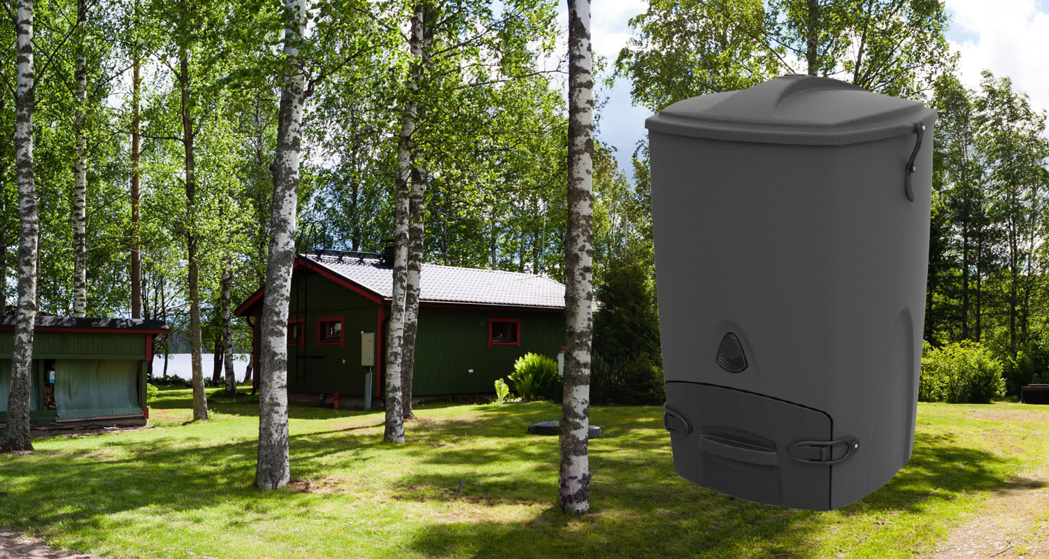 Metsämaisemassa vihreä mökki punaisin yksityiskohdin koivujen keskellä, edessä musta kompostisäiliö