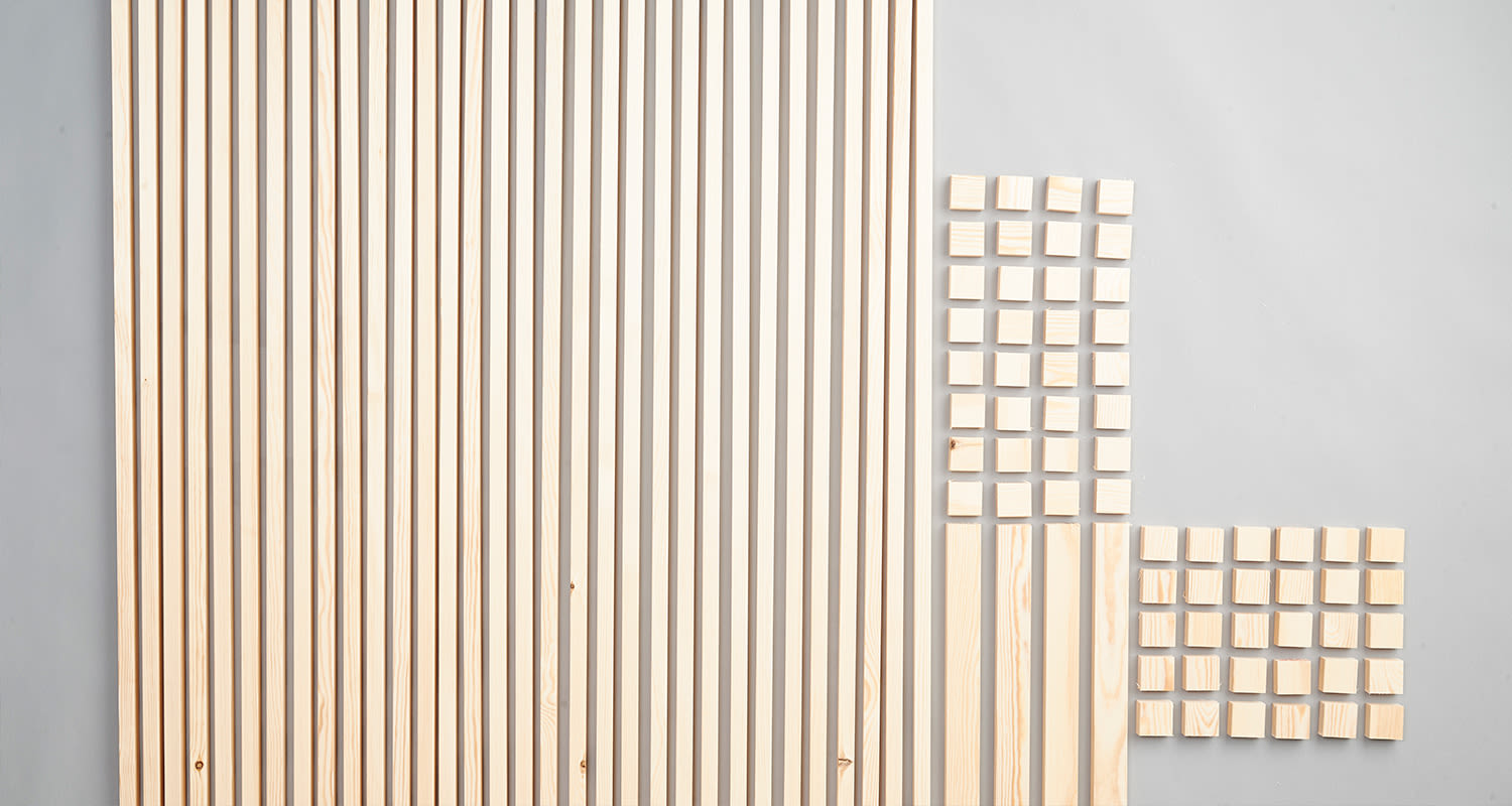 Vaaleita pystysuoria puulistoja harmaalla pinnalla ja kaksi ryhmää pieniä puuneliöitä.