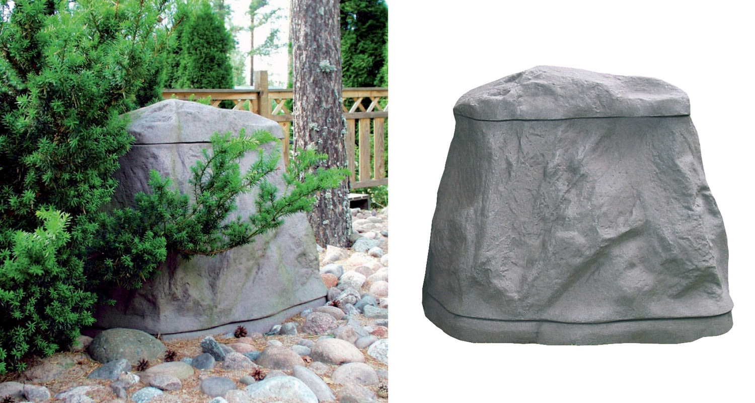 Harmaa kiveä muistuttava kaiutinpeite puutarhan kivikossa vihreiden pensaiden keskellä.